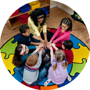 Preschool teacher with 6 preschoolers sitting on the floor with their hands all stretched out arms and hands on top of each other.