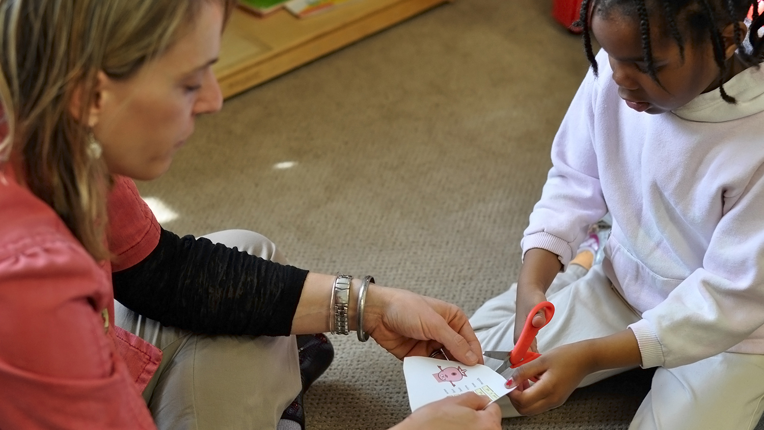 Teacher helping young student using sissors.