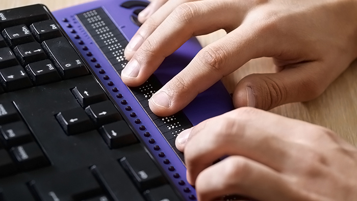 Blind person using a computer with a braille computer display and computer keyboard.