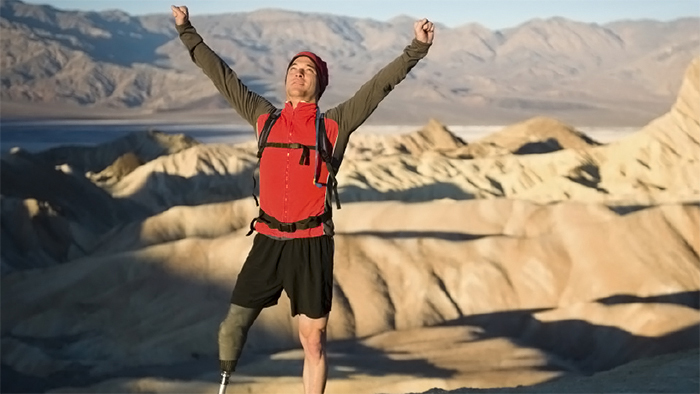 Hiker with an artifical leg reaches the top of a mountain.