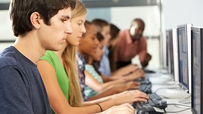 Group Of Students Working At Computers In Classroom Typing On Keyboard