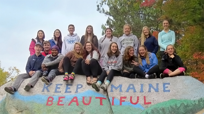 Group of teens sitting on top of large granite boulder with the words, Keep Maine Beautiful painted on it.