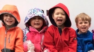 Four preschoolers smiling wearing their coats with hoods.
