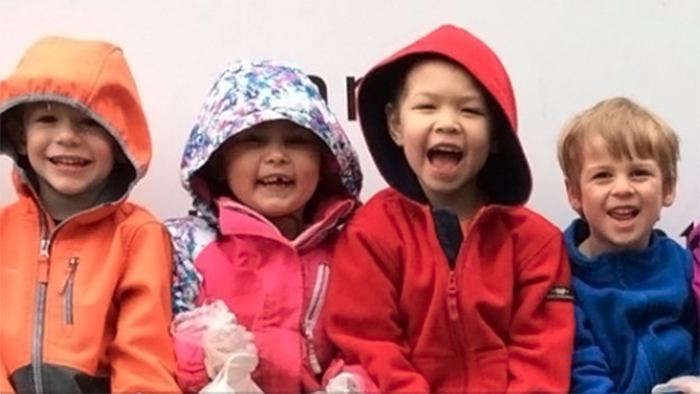 Four preschoolers smiling wearing their coats with hoods.