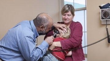 Mother holding child while doctor looks in his ear.