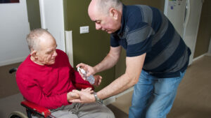 Suppot staff assisting a man in a wheelchair with hand sanitizer.