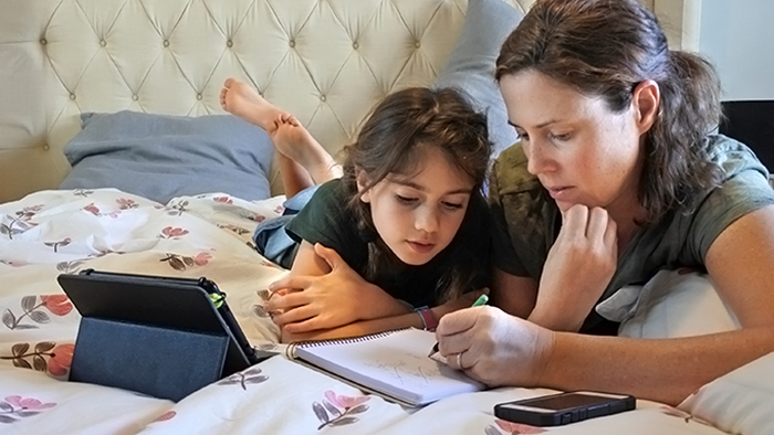 School-aged daughter and her mother doing homework together in a bedroom.