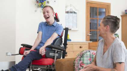 Young Adult man in a wheelchair in his living room with his mother.