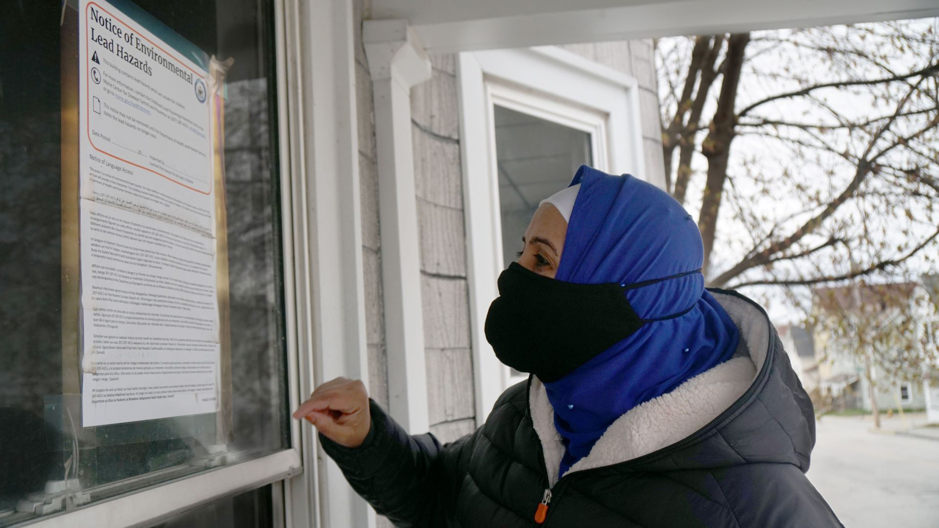 Hibo Omer standing outside a house on Maple Street in Lewiston, Maine, reading an official notice of environmental lead hazards taped to the front door.