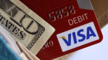 The corners of a U.S. ten-dollar bill and a red VISA debit card sticking out of a blue wallet.