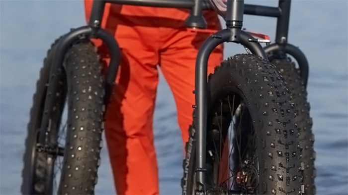 A person with orange pants walking along the shoreline using an Off-Road Afari, a three-wheeled mobility device.