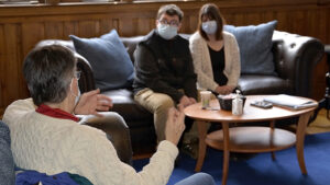 Janet May speaking to Jake Rousseau and Christy Rousseau (all masked) while seated in the Heritage House waiting room.