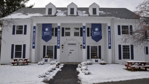 The exterior of the historic Heritage House, a two-story building with white clapboard siding on the University of Maine campus in Orono, ME.