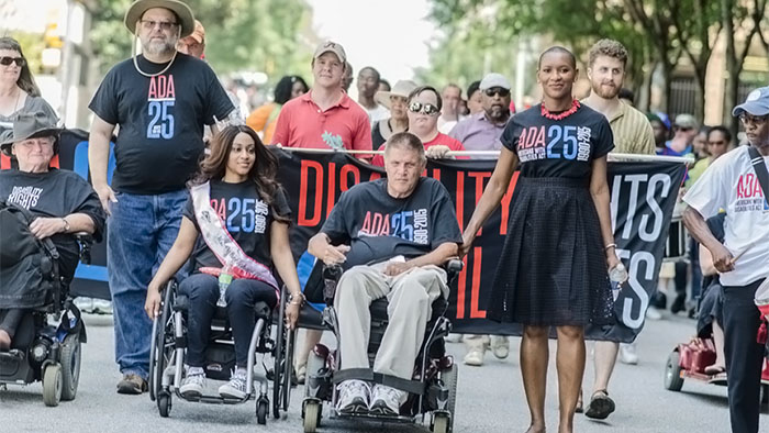 Individuals with and without disabilities wearing black t-shirts that readADA25th 1990-2015marching in the street to celebratethe 25th anniversary of the Americans with Disabilities Act.