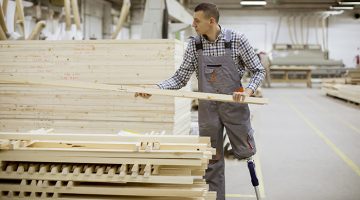 Young man with a prosthetic leg moving lumber in a warehouse.