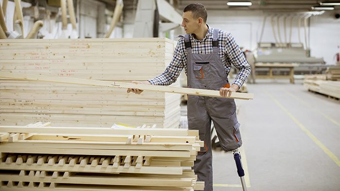 Young man with a prosthetic leg moving lumber in a warehouse.