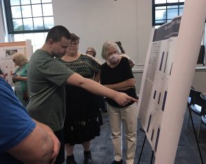 Male student pointing at his poster with his instructor and her advisor looking on.