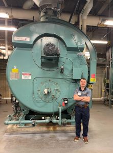 Zachery Johnson standing next to a boiler at MaineGeneral..