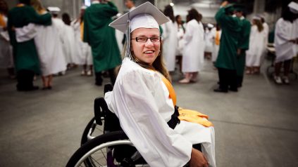 A female college student in her wheelchair dressed in her graduation gown.