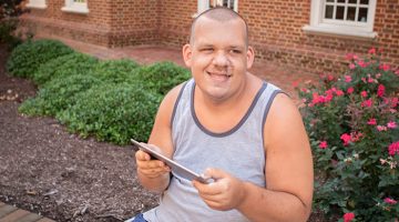 Man with autism using a tablet while sitting outdoors on a bench.