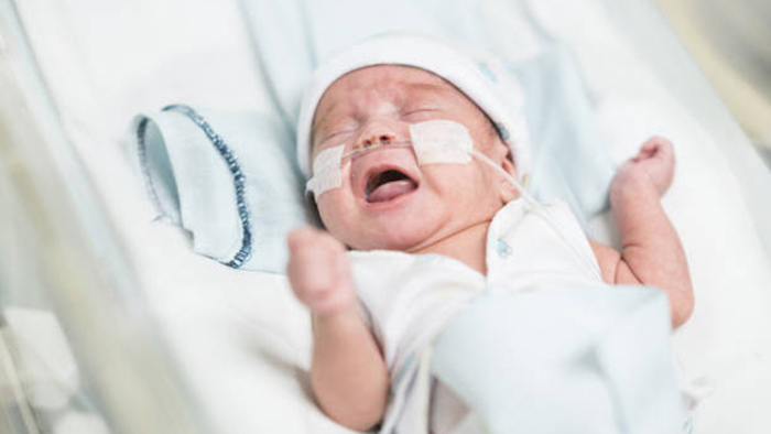 Beautiful premature baby boy in an incubator at neonatal intensive care unit with oxygen crying.