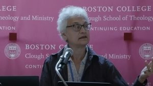 Woman with white hair and glasses speaking from a podium at Boston College's Clough School of theology and Ministry in June 2024.